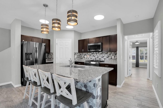 kitchen with hanging light fixtures, a kitchen breakfast bar, backsplash, a center island with sink, and appliances with stainless steel finishes