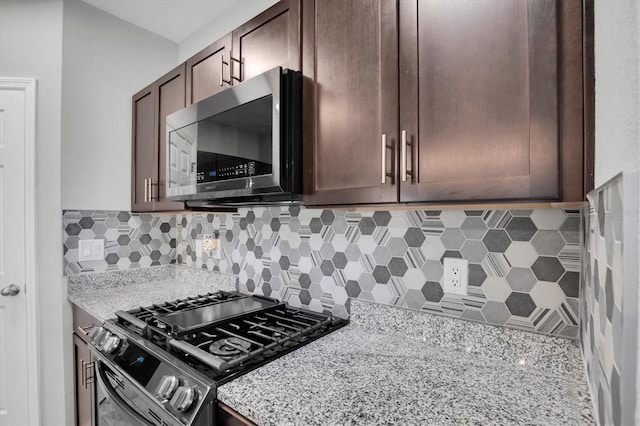 kitchen with decorative backsplash, light stone counters, dark brown cabinets, and stainless steel appliances