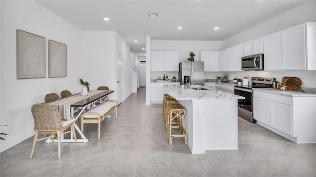 kitchen with light stone countertops, a kitchen breakfast bar, a kitchen island with sink, white cabinets, and appliances with stainless steel finishes