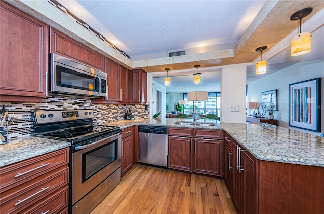 kitchen with light hardwood / wood-style floors, stainless steel appliances, hanging light fixtures, kitchen peninsula, and sink