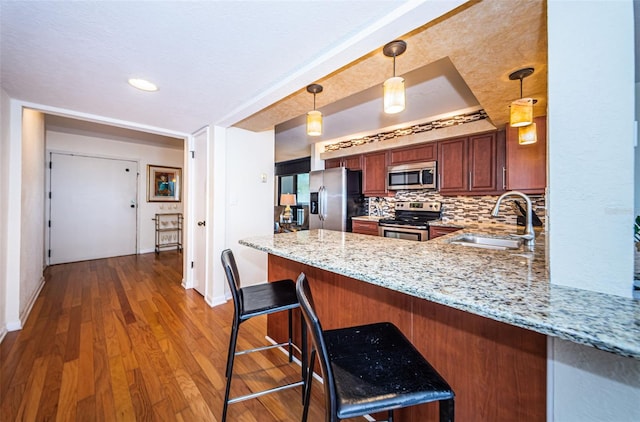 kitchen featuring appliances with stainless steel finishes, kitchen peninsula, pendant lighting, a breakfast bar, and sink