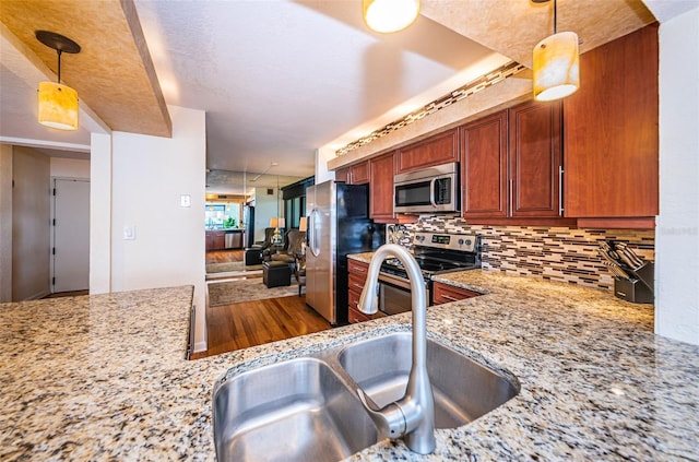 kitchen with sink, decorative light fixtures, decorative backsplash, light stone countertops, and appliances with stainless steel finishes