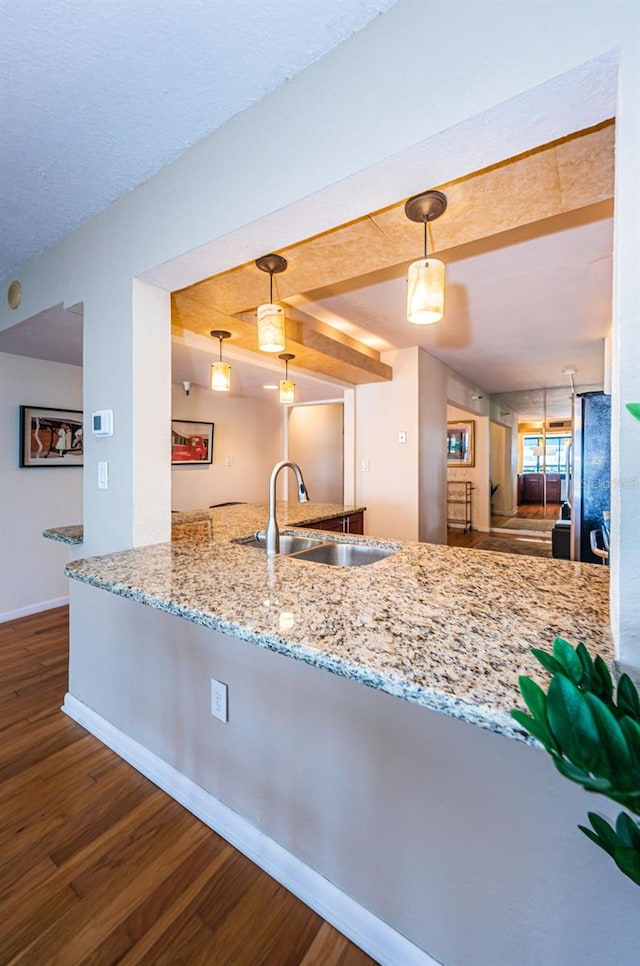 kitchen with sink, hanging light fixtures, light stone countertops, dark hardwood / wood-style flooring, and stainless steel fridge