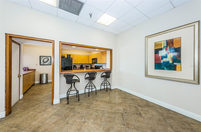 kitchen featuring a paneled ceiling, a breakfast bar area, black appliances, and kitchen peninsula