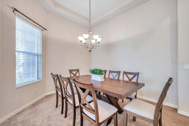 dining space with light colored carpet, a tray ceiling, and a chandelier