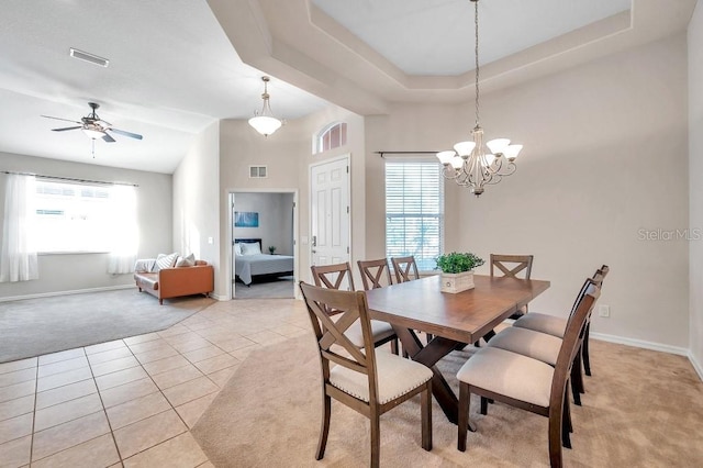 dining area with light tile patterned floors, ceiling fan with notable chandelier, and a raised ceiling