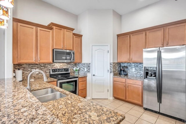 kitchen with sink, stainless steel appliances, a towering ceiling, decorative backsplash, and light tile patterned flooring