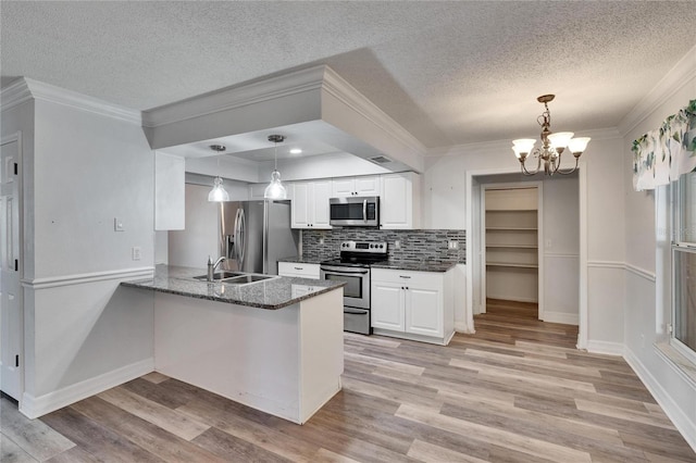 kitchen featuring white cabinets, hanging light fixtures, appliances with stainless steel finishes, kitchen peninsula, and a chandelier