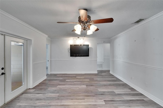 interior space featuring a textured ceiling, light wood-type flooring, crown molding, and french doors