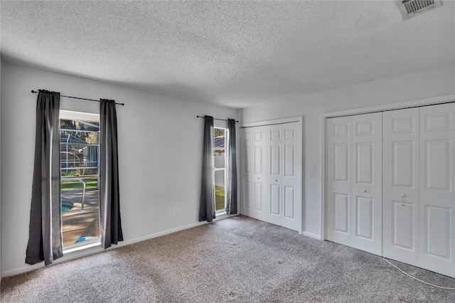 unfurnished bedroom with a textured ceiling, carpet floors, and two closets