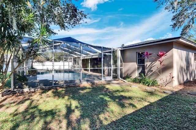 rear view of house with a lawn, glass enclosure, and a fenced in pool