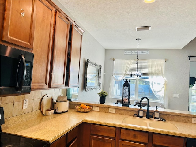 kitchen with stove, sink, hanging light fixtures, decorative backsplash, and a textured ceiling