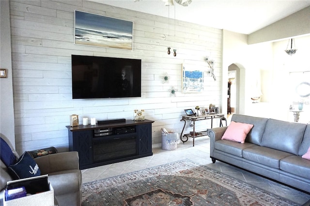 living room featuring light tile patterned floors, ceiling fan, lofted ceiling, and wood walls