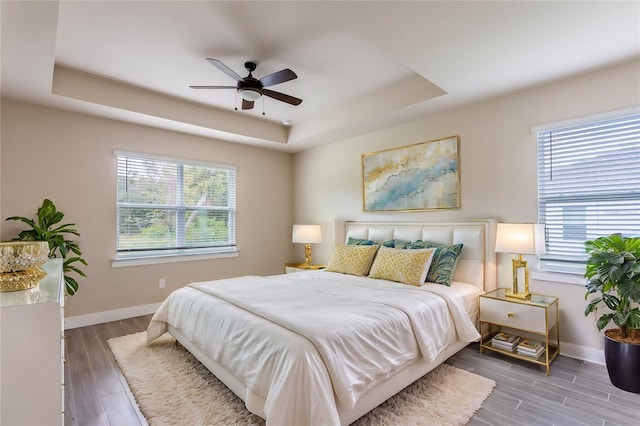 bedroom featuring a tray ceiling, multiple windows, ceiling fan, and hardwood / wood-style flooring