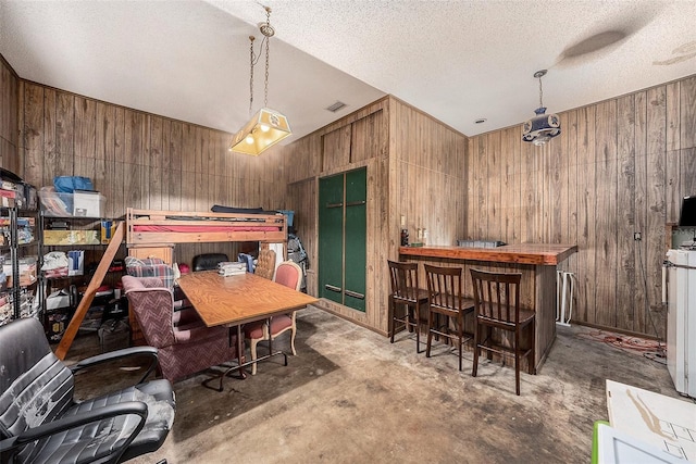 dining space featuring a textured ceiling, wooden walls, and concrete floors