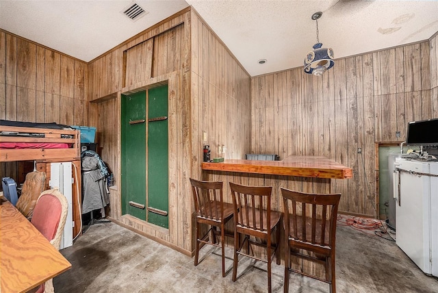 dining space with bar, a textured ceiling, and wooden walls