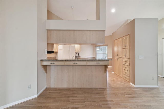 kitchen featuring white fridge, light brown cabinets, light hardwood / wood-style floors, kitchen peninsula, and a high ceiling