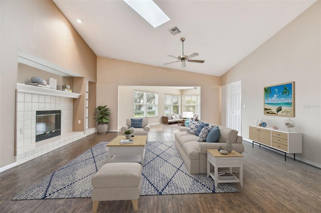 living room featuring a fireplace, ceiling fan, vaulted ceiling with skylight, and dark hardwood / wood-style floors