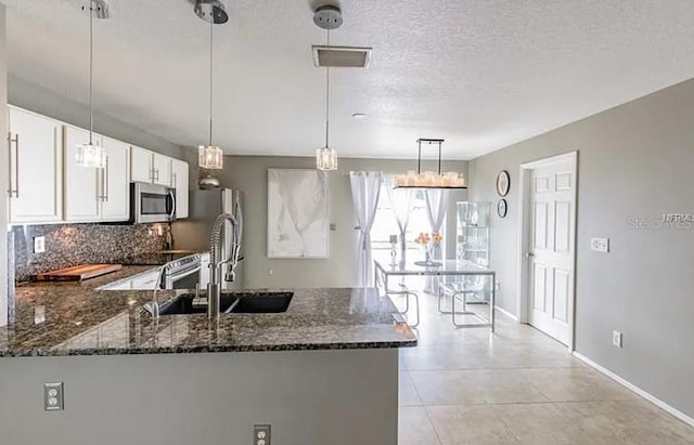 kitchen featuring stainless steel appliances, dark stone countertops, kitchen peninsula, decorative backsplash, and white cabinets