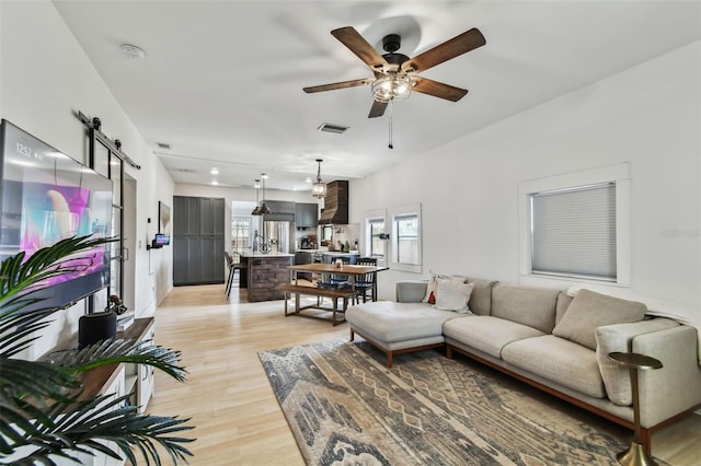 living room with ceiling fan, a barn door, and light hardwood / wood-style flooring