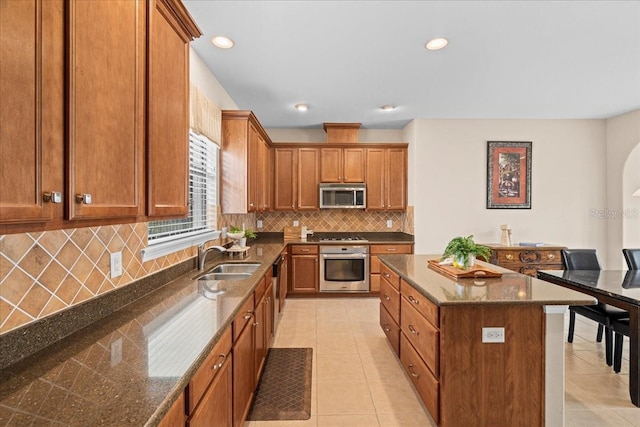 kitchen with a center island, stainless steel appliances, dark stone counters, sink, and light tile patterned floors