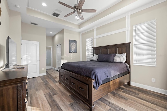 bedroom featuring crown molding, ceiling fan, a tray ceiling, dark hardwood / wood-style flooring, and a closet