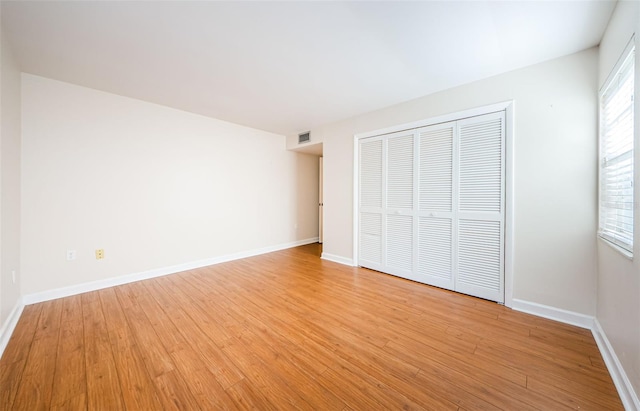 unfurnished bedroom featuring multiple windows, light hardwood / wood-style flooring, and a closet