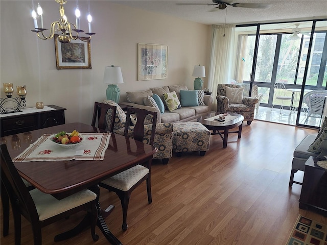 living room with ceiling fan with notable chandelier, light wood-type flooring, and a wall of windows