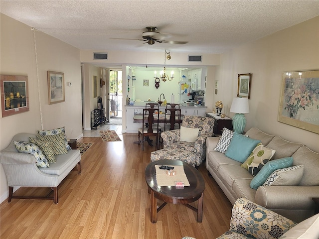 living room with ceiling fan with notable chandelier, light hardwood / wood-style floors, and a textured ceiling