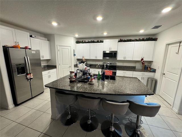 kitchen featuring light tile patterned floors, a center island with sink, appliances with stainless steel finishes, and white cabinets