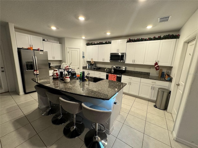 kitchen with white cabinets, an island with sink, light tile patterned floors, and stainless steel appliances