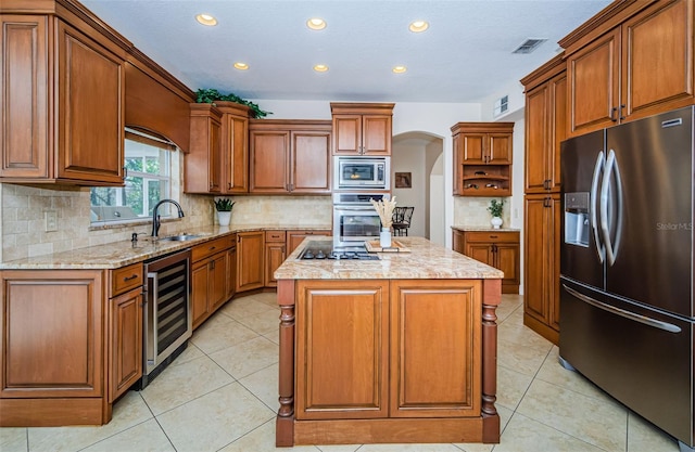 kitchen featuring appliances with stainless steel finishes, an island with sink, sink, beverage cooler, and decorative backsplash