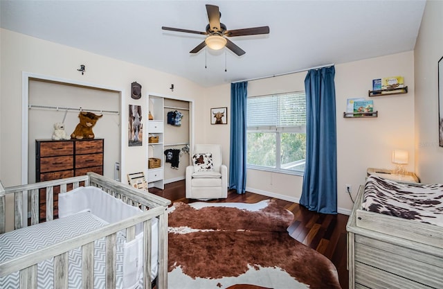 bedroom featuring a nursery area, ceiling fan, and dark wood-type flooring