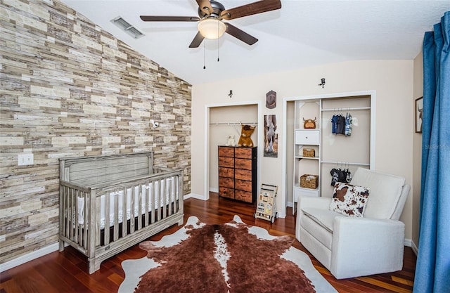 bedroom featuring lofted ceiling, a crib, dark hardwood / wood-style floors, and ceiling fan