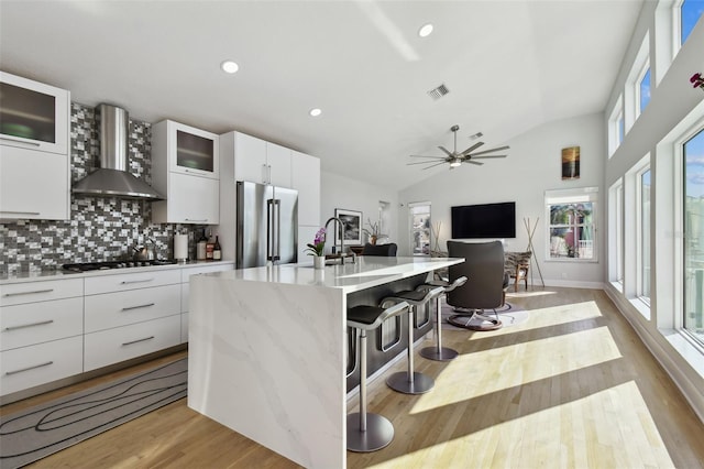 kitchen featuring white cabinets, high end fridge, wall chimney range hood, and vaulted ceiling