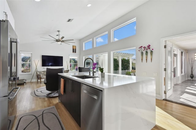 kitchen featuring a center island with sink, sink, ceiling fan, light wood-type flooring, and stainless steel appliances