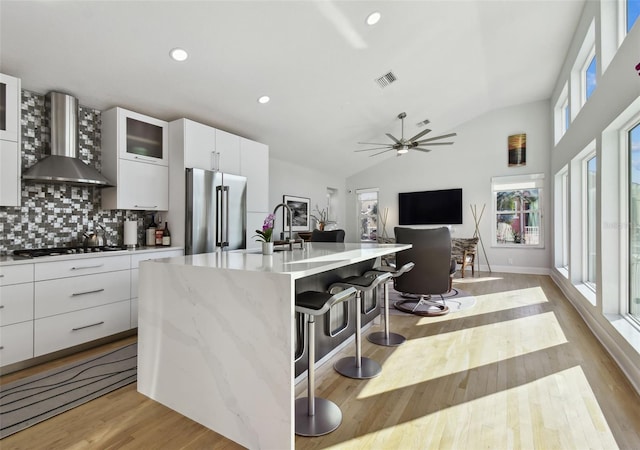 kitchen with backsplash, high end fridge, a breakfast bar, wall chimney range hood, and lofted ceiling