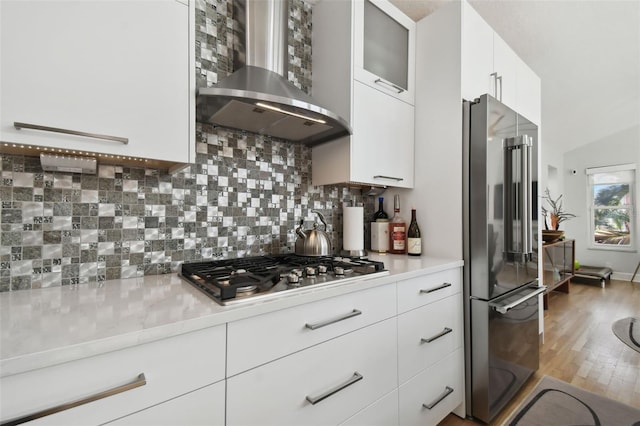 kitchen with white cabinetry, stainless steel appliances, wall chimney range hood, backsplash, and wood-type flooring