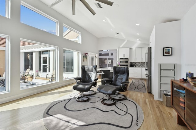 sitting room with a healthy amount of sunlight, high vaulted ceiling, and light hardwood / wood-style floors