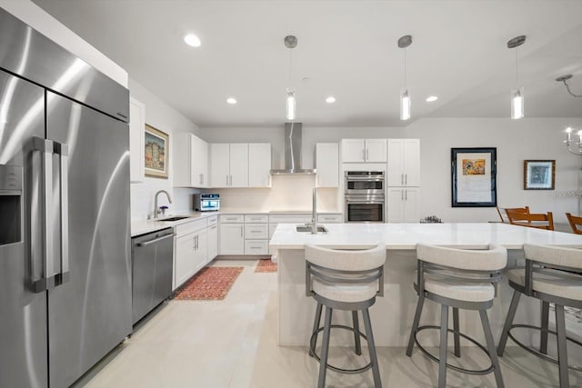 kitchen with stainless steel appliances, wall chimney range hood, decorative light fixtures, white cabinets, and a kitchen island