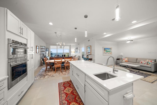 kitchen featuring pendant lighting, sink, an island with sink, double oven, and white cabinetry