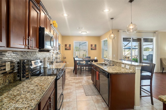 kitchen with light stone countertops, a breakfast bar, stainless steel appliances, pendant lighting, and light tile patterned floors