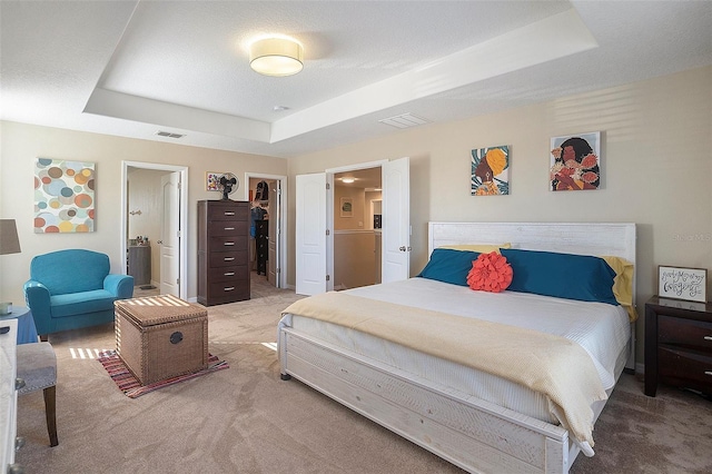 carpeted bedroom with ensuite bathroom, a walk in closet, a textured ceiling, a tray ceiling, and a closet