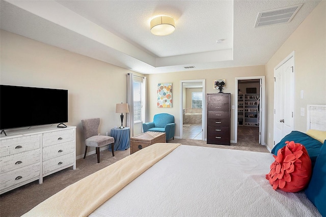 bedroom featuring a raised ceiling, ensuite bathroom, carpet floors, a walk in closet, and a closet