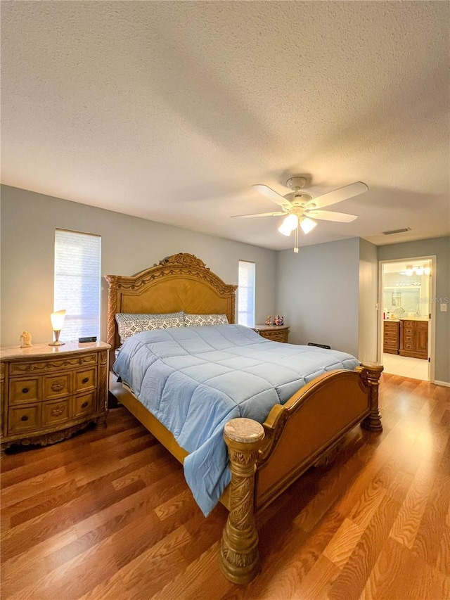 bedroom with ceiling fan, ensuite bath, a textured ceiling, and hardwood / wood-style flooring