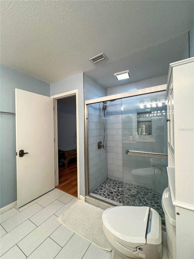 bathroom featuring walk in shower, tile patterned flooring, toilet, and a textured ceiling