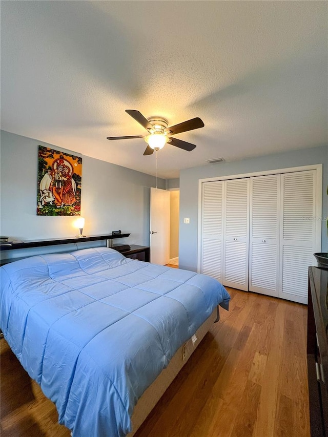 bedroom with a textured ceiling, ceiling fan, a closet, and hardwood / wood-style floors