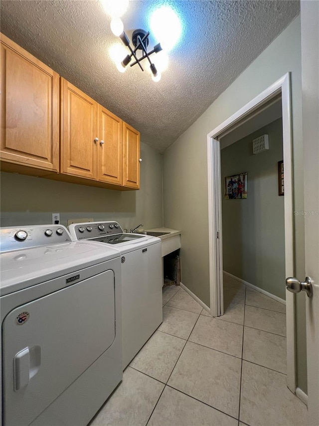 laundry room featuring sink, washing machine and clothes dryer, a textured ceiling, light tile patterned floors, and cabinets