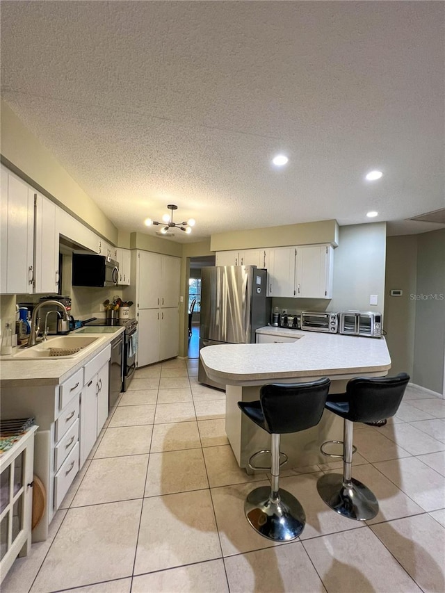 kitchen with white cabinets, appliances with stainless steel finishes, sink, a breakfast bar, and light tile patterned floors