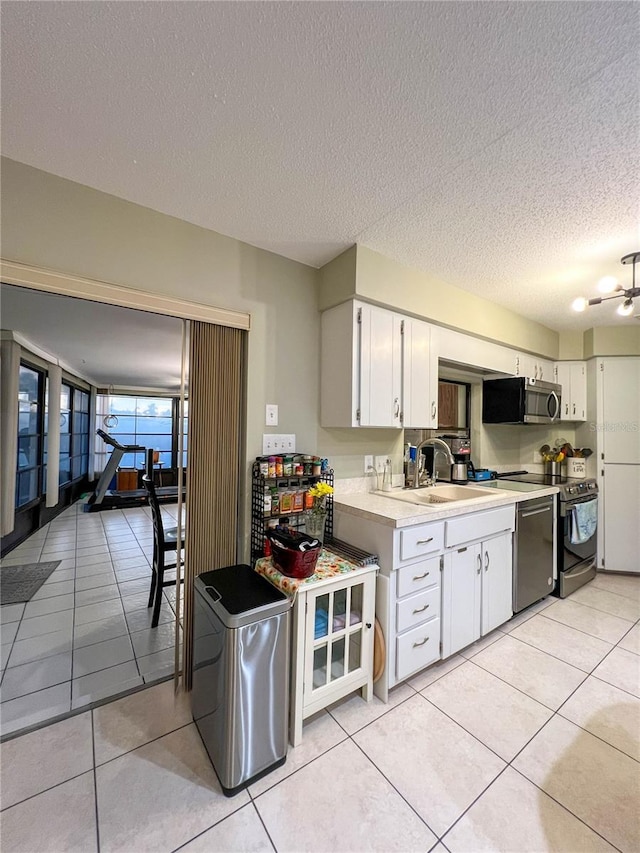 kitchen with light tile patterned flooring, sink, white cabinetry, a textured ceiling, and stainless steel appliances